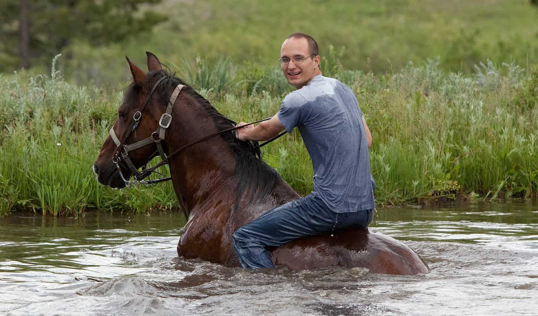 Young Man Crossing The River With Horse Swimming